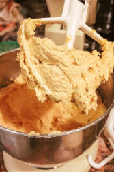 A stand mixer attachment covered in cookie batter above a metal mixing bow.