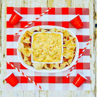A red and white checkered placemat topped with a white oval serving dish filled with Rotel Dip and tortilla chips.