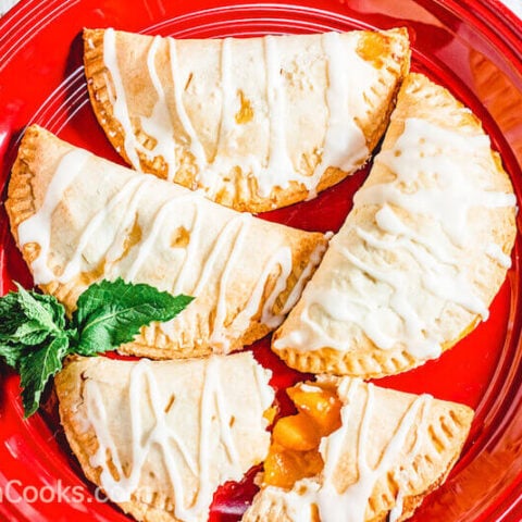 A red plate filled with 4 peach hand pies that are drizzled with icing.