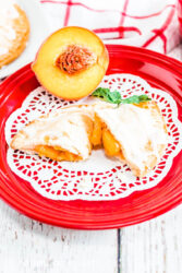 Close up of a peach hand pie cut in half, on top of a doily on a red plate.