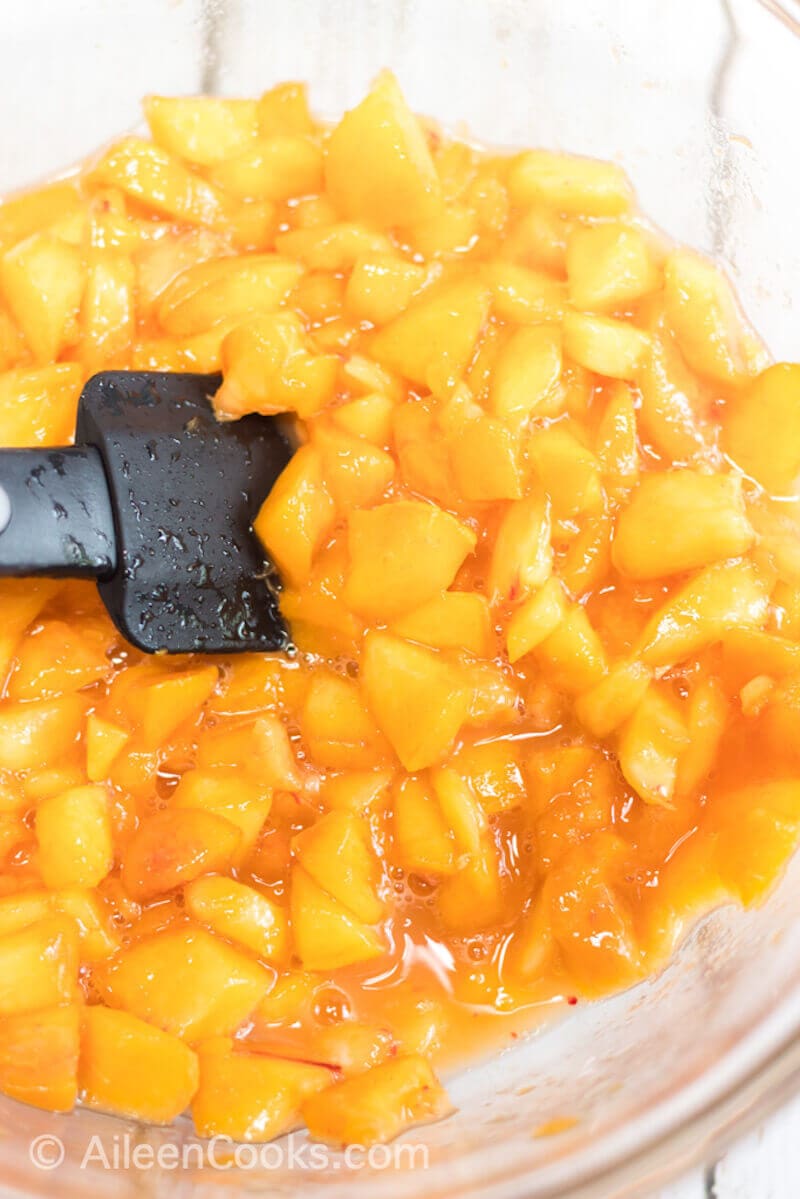 Diced peaches being stirred with a black spoon.