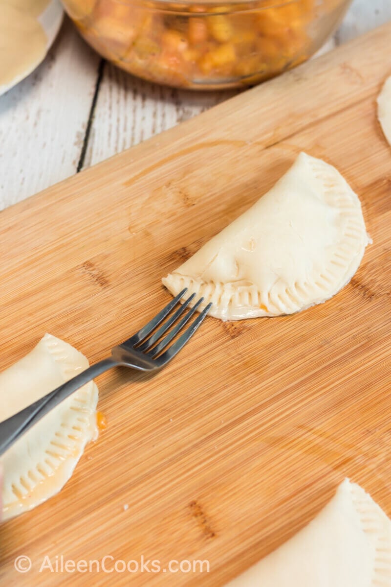 A fork crimping the edges of a hand pie on a wooden cutting board.