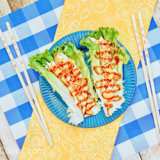 A blue plate of lettuce wraps on top of a yellow cloth.