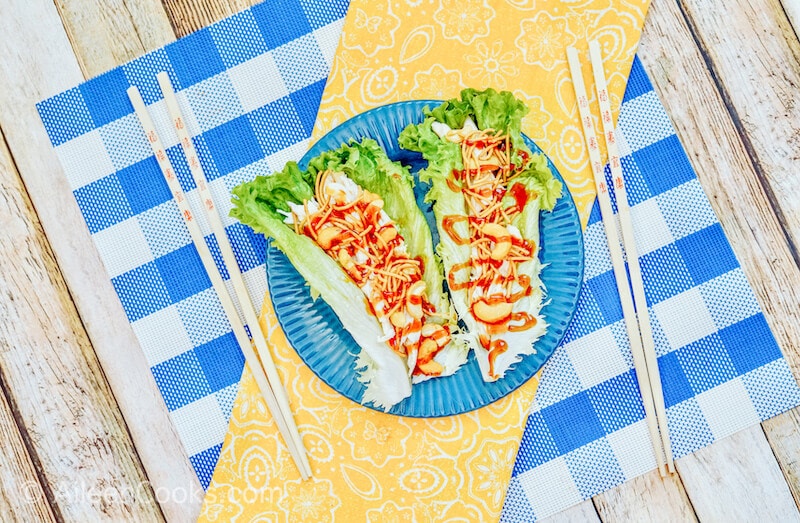 A blue plate of lettuce wraps on top of a yellow cloth.