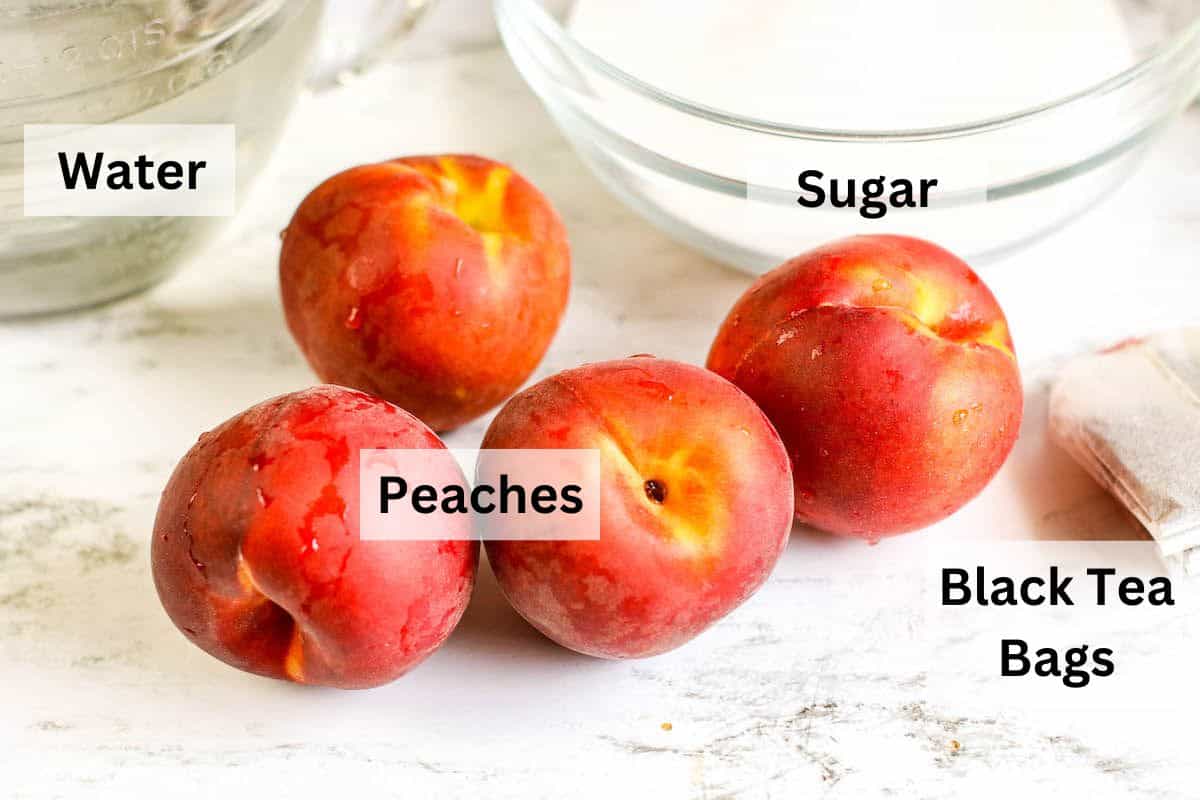 Four peaches on a white counter top next to a stack of tea bags and a bowl of sugar.