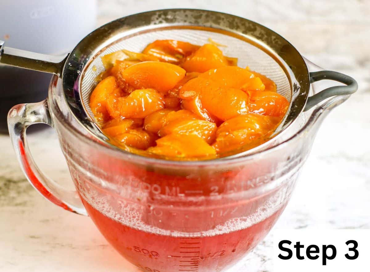 A glass measuring cup fitted with a strainer of cooked peaches and peach syrup.