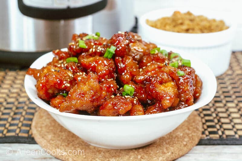 An instant pot with a bowl of general tso's chicken in front of it.