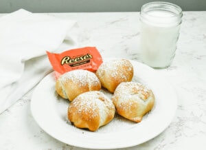 A white plate of four air fried Reeses next to a glass of milk.