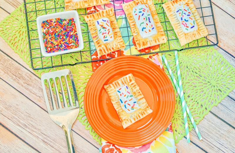 A cooling rack of pop tarts above an orange plate with a pop tart.