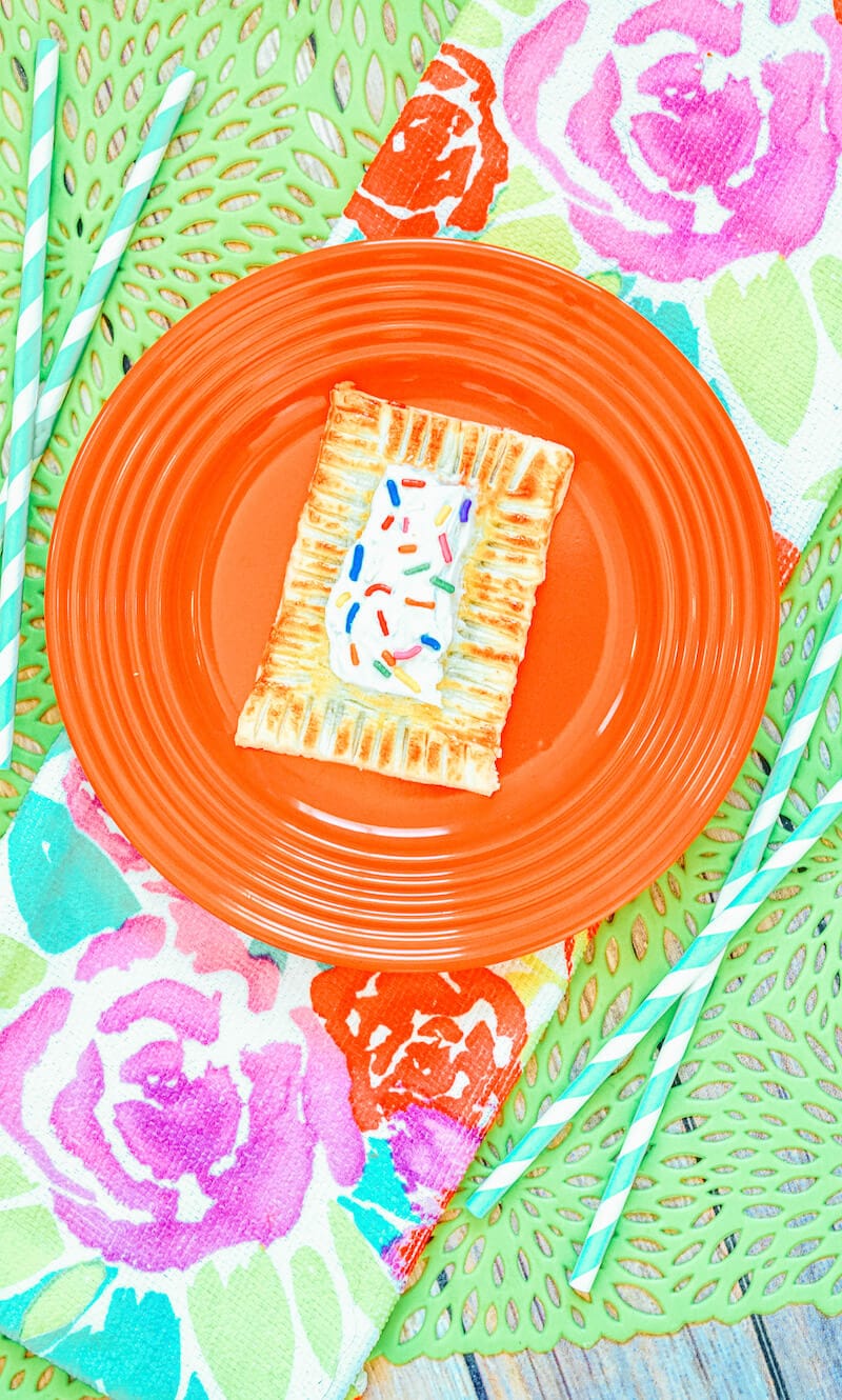 A floral tablecloth topped with an orange plate with a pop tart.
