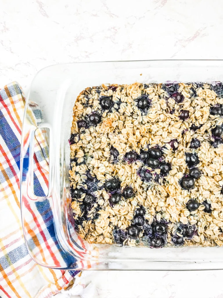 A glass dish of blueberry baked oatmeal next to a striped towel.