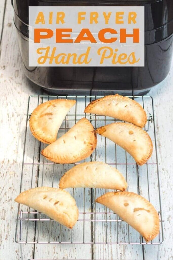 A cooling rack of hand pies in front of an air fryer with the words "air fryer peach hand pies" in orange lettering.