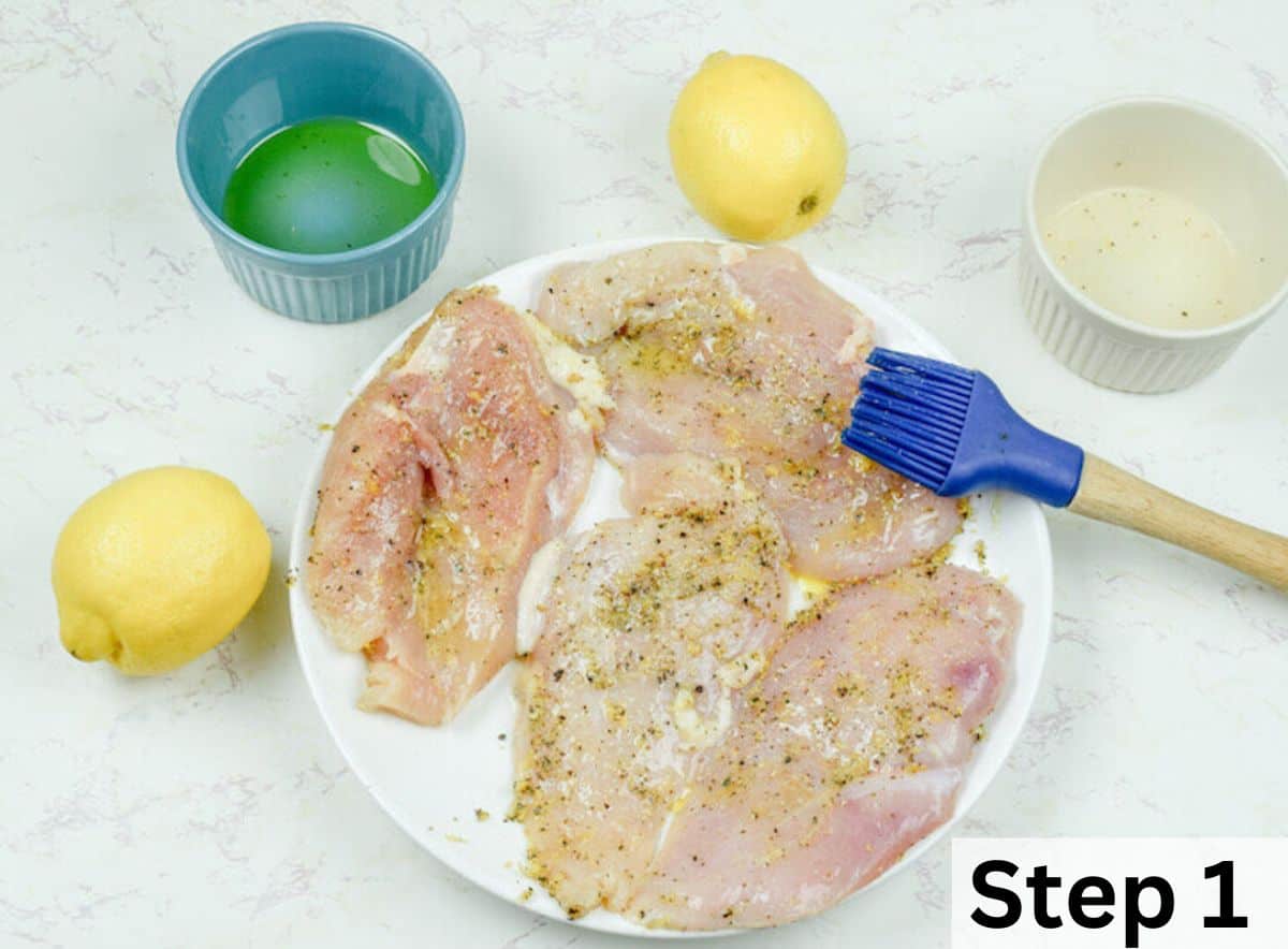 A white plate filled with thin sliced chicken breasts covered in lemon juice and seasoning.
