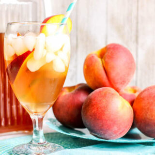 A glass of iced tea next to a plate of fresh peaches.