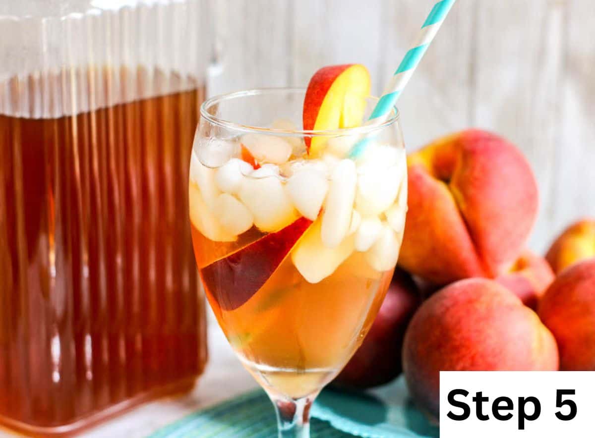 A glass of iced tea with sliced peaches and a blue striped straw.