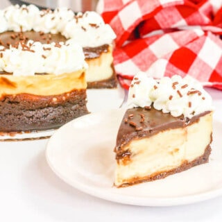 A slice of brownie cheesecake on a white plate next to the whole cheesecake.