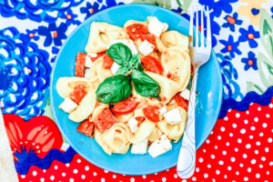 A blue plate of pepperoni pasta salad topped with fresh basil.