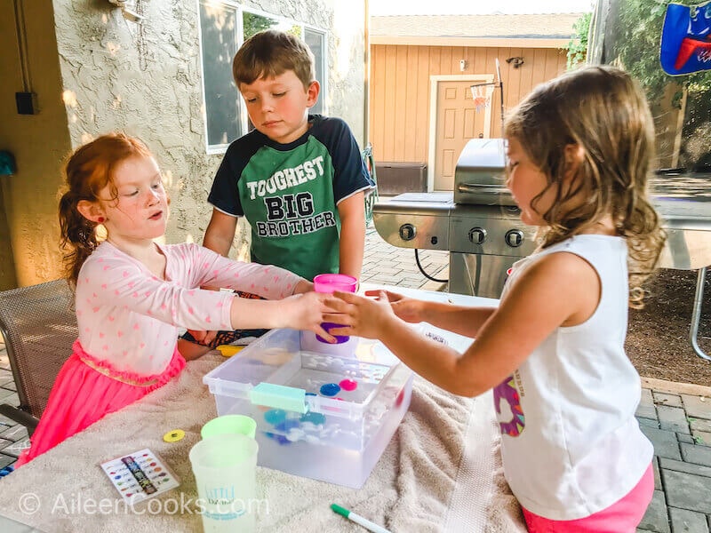 Three kids passing around cups of pretend juice.