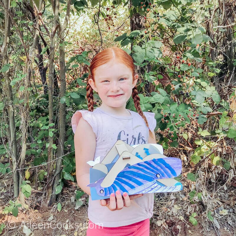 A girl standing outside holding a whale shaped mechanical sweeper.