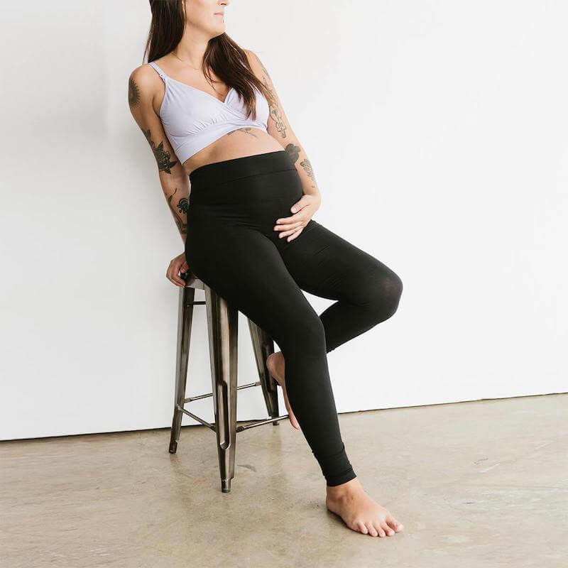 Woman in black leggings leaning on a stool and holding her pregnant belly.