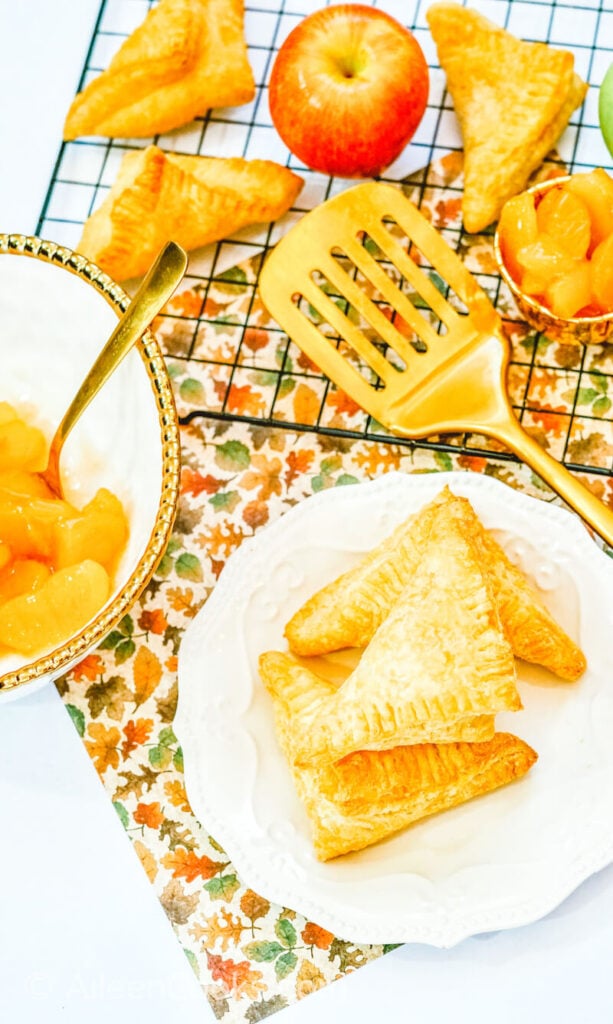 A cooling rack of air fryer apple hand pies next to a plate of hand pies.