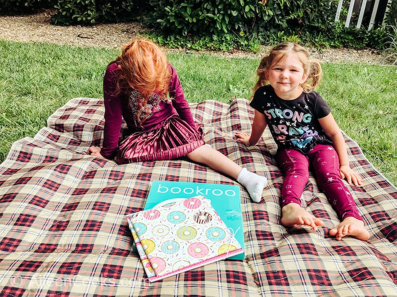 Two girls sitting together outside next to a Bookroo box.