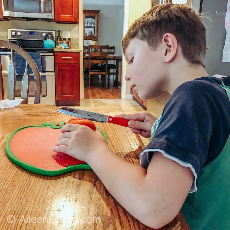 A boy slicing a tomato with a knife.