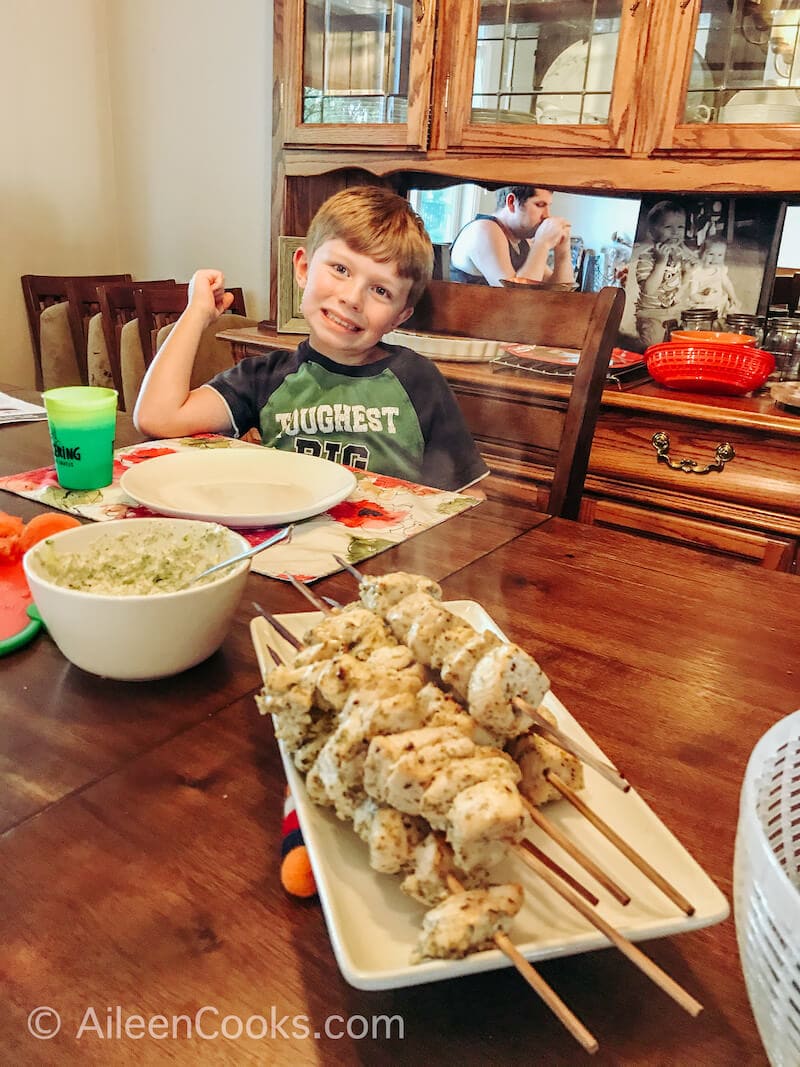 A tray of chicken skewers in front of a smiling boy.