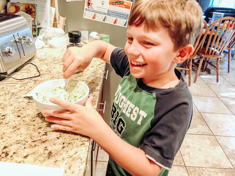 A boy staring a white bowl of sauce and smiling.
