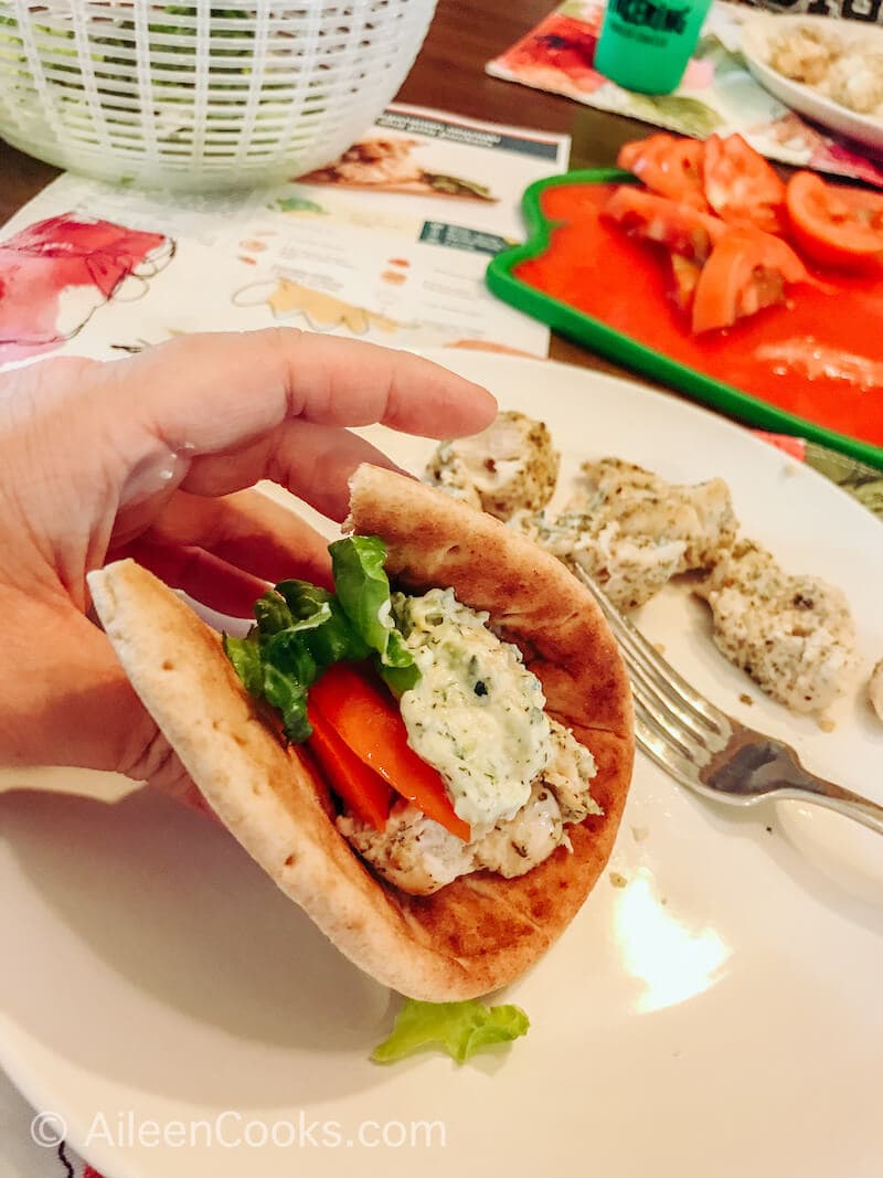 A hand holding up a pita filled with chicken, tzaziki, tomato, and lettuce.e