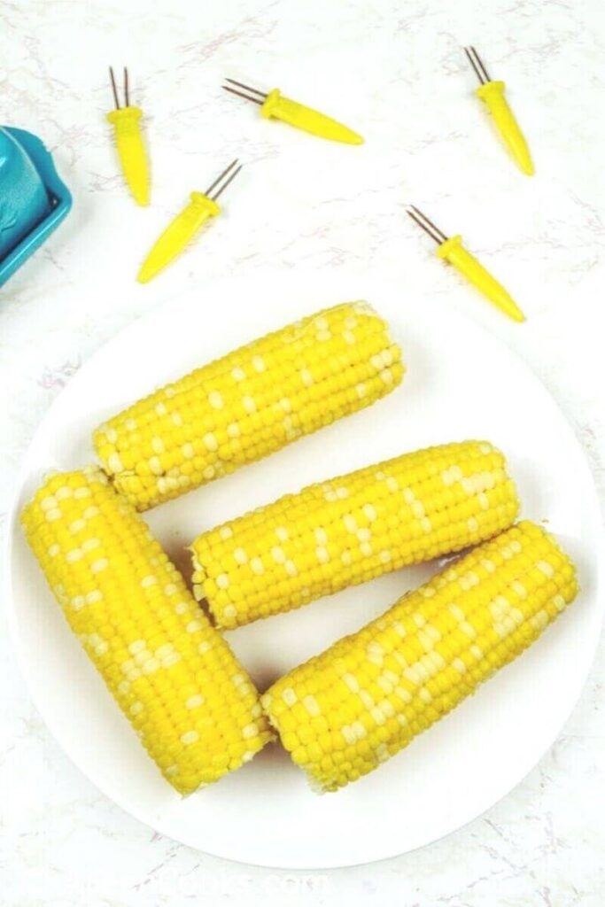 Overhead shot of 4 ears of corn on the cob next to a blue butter dish.