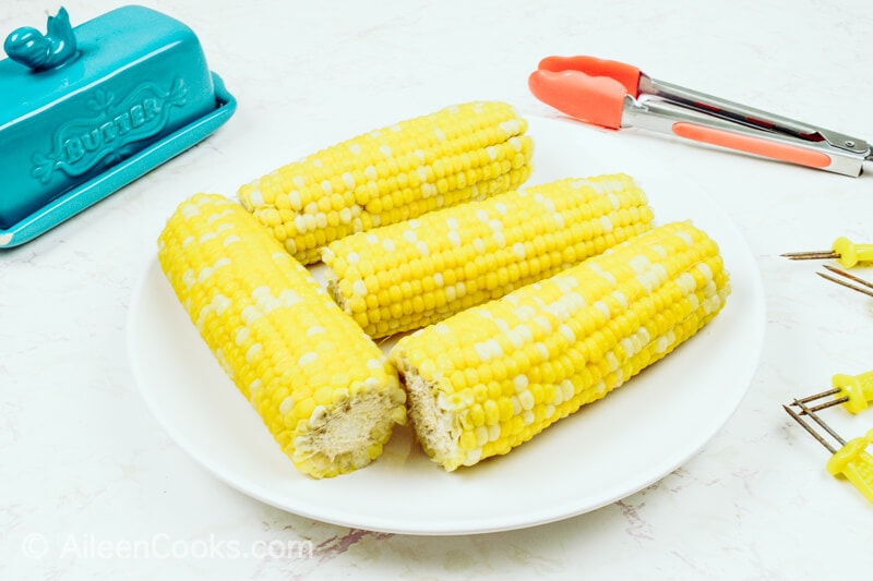 A white plate with four ears of corn on the cob, next to a blue butter dish.