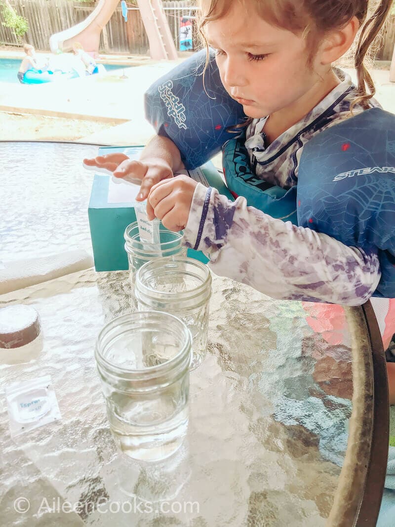 A little girl pouring seeds into a glass of water.