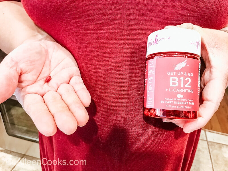 A hand holding a B12 tablet with the other hand holding the bottle.