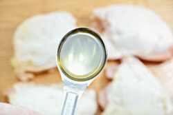 A tablespoon of oil held above four raw chicken thighs.