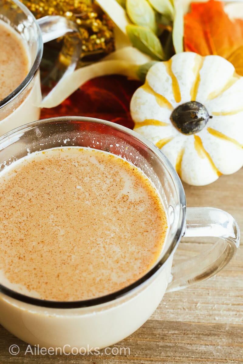 A pumpkin spice latte in front of two small pumpkins.