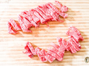 Steak cut into thin strips on a wooden cutting board.