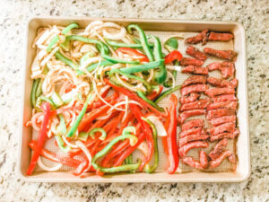 Sliced steak and vegetables on a cookie sheet.
