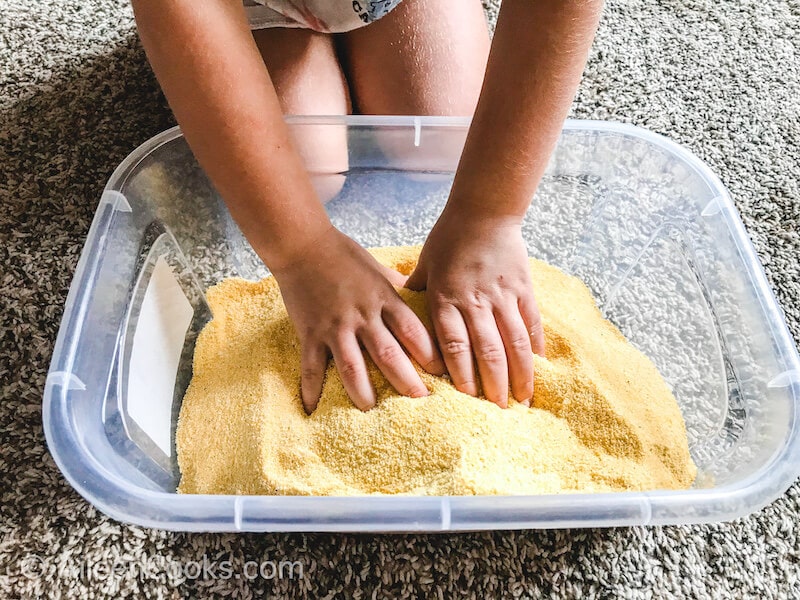 A plastic bin of cornmeal with two child's hands inside.