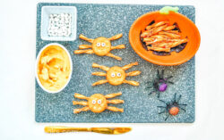 Spider decorated crackers with candy eyes, on a grey cutting board.