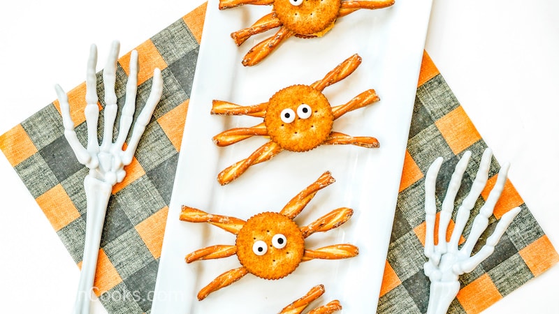 Halloween spider crackers on a white platter next to two fake skeleton arms.