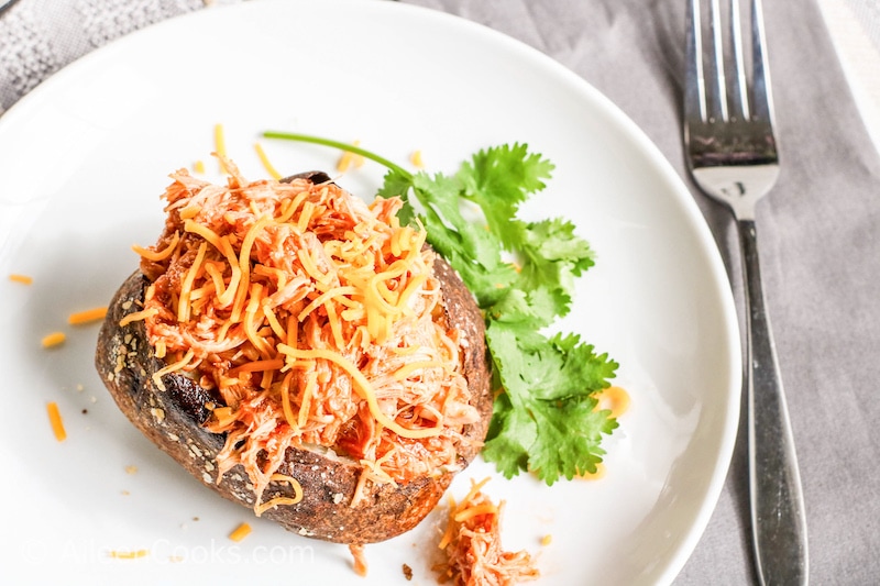 A loaded baked potato next to a sprig of parsley on a white plate.