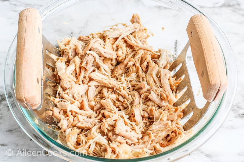 Chicken thighs shredded in a glass bowl.