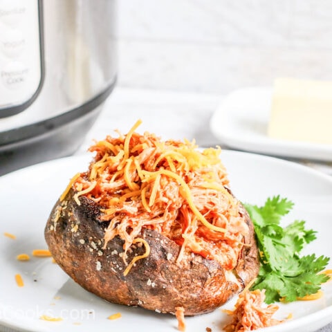 Side view of baked potato loaded with barbecue chicken in front of instant pot.