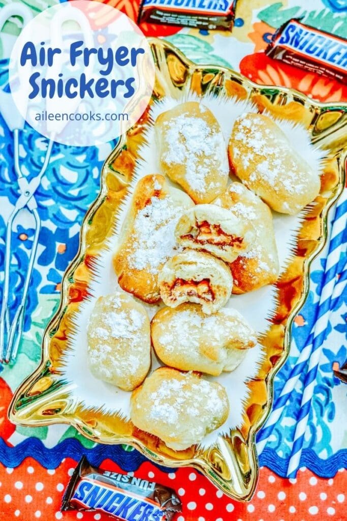 A platter of air fried snickers coated in powdered sugar with the words "air fryer snickers" in blue lettering.