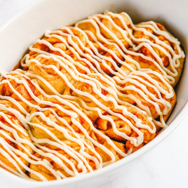 Pumpkin cinnamon rolls in a baking dish with frosting on top