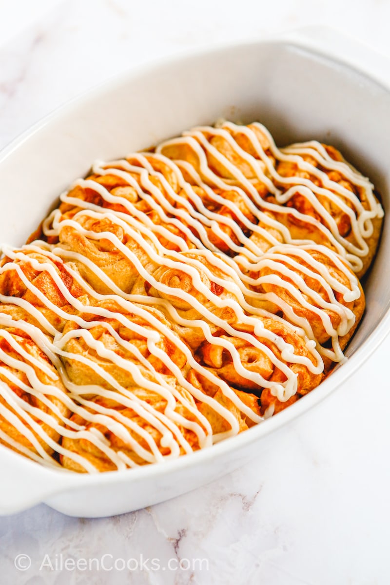 Pumpkin cinnamon rolls in a baking dish with frosting on top