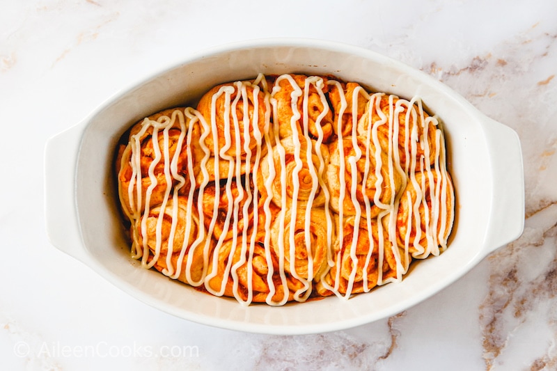 Pumpkin cinnamon rolls in a baking dish with frosting on top