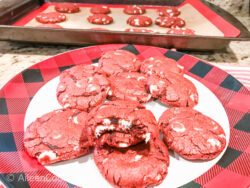 A plate of red velvet cookies in front of a cooling rack filled with cookies.