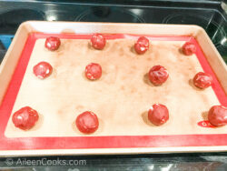 Red Velvet cookie dough balls on a cookie sheet.